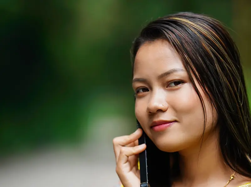 A smiling young Indian woman in a yellow kurta talking on her phone outdoors