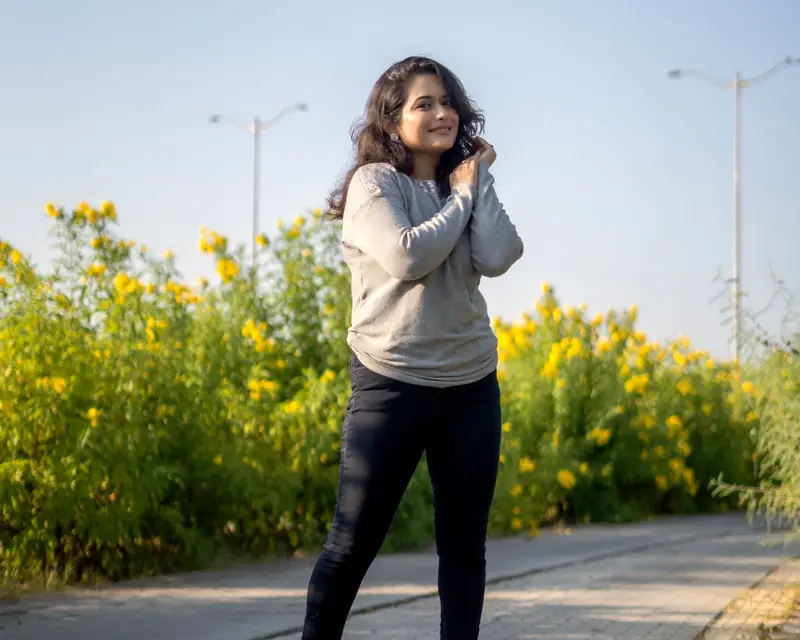 A smiling young Indian woman on a sunny morning walk beside yellow flowers